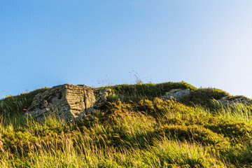 Boulders and rocks in the mountains. Carpathians. Summer, Autumn, Spring. The grass is influenced by the wind. Monument at the top of the mountain. Sunny weather.