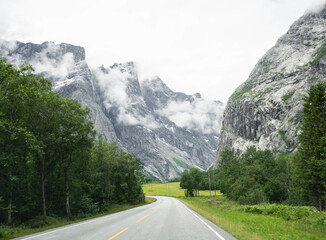 View of an empty paved road with white lines. Mountain road through a valley with trees and green lawns