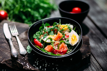 Salad with salmon, arugula and egg in a black plate 