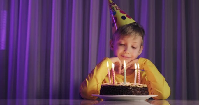 Cute boy blows out candles on a cake on his birthday.  Happy child looks at a cake with candles. Child looks at the cake and makes a birthday wish. Boy celebrates his birthday. Happiness concept