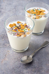 Top closeup of two glasses with natural yogurt, biscuit pieces and colors, on gray background and spoon, in vertical