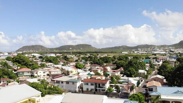 Aerial shot of Independence Square in Basseterre, St. Kitts and Nevis. Drone flying backwards from residential houses area, over the cathedral and revealing trees and fountain