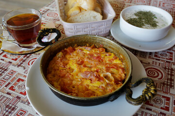Menemen, a traditional Turkish dish, made with eggs, tomato, green pepper and a variety of spices, accompanied by bread, black tea and Cacik, yogurt with cucumbers and herbs served in a restaurant.