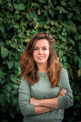Obraz premium Portrait of a young brunette woman with long hair on a background of green leaves