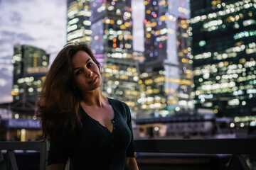 A young woman stands at night in front of glowing glass skyscrapers in Moscow. High ISO, grainy and noisy images.