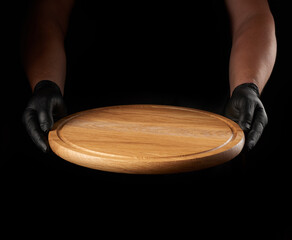 male hands in black latex gloves holds round empty wooden pizza board