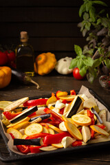 Fresh vegetables ready for roasting in the oven, eggplant and zucchini, bell peppers and onions with spices, vegetables on a baking sheet on a wooden background