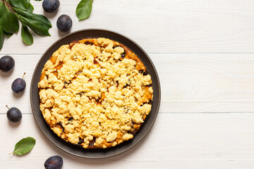 Delicious juicy plum cake in a round plate on a white wooden background, plum tree leaves with fruits