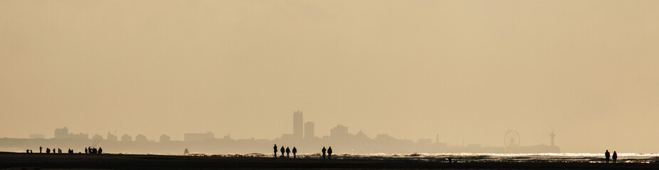 The Hague, Netherlands, beach and skyline in strong backlight; unidentifiable people walk along the...