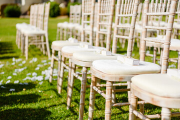 Closeup on wedding decorated empty wooden chairs for guests on green grass. Sunny day time outdoors background.