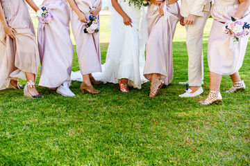 Bride, bridesmaids, bridegroom and groomsmen show off their shoes at wedding party celebration on summer green grass outdoors background.