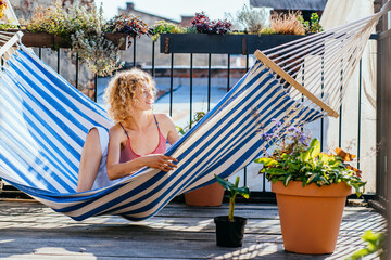Positive woman lie down comfortably hammock. Girl sunbathing under bright scorching sun on hammock,...