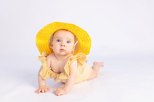 Smiling Baby Girl 6 Months Old In A Swimsuit And Sun Hat Lying On A White Isolated Background, Space For Text