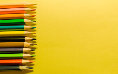 set of multi-colored pencils on a yellow isolated background with space for text