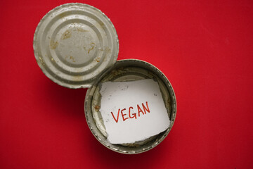 Opened empty  tin can with note with the inscription - VEGAN ?  red background.