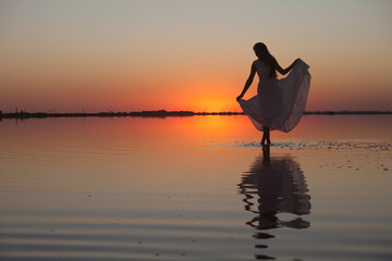 Woman silhouette in a beautiful dress on the lake in the evening light at sunset