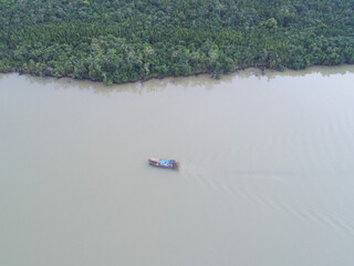 Aerial view. Boat sailing across river with rainforest at river bank