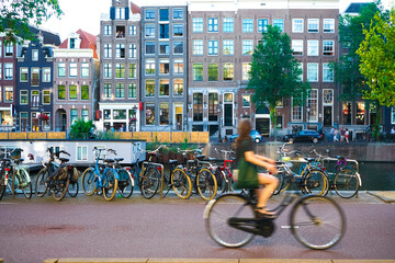 Young blurred woman in green dress with bag riding a bicycle in Amsterdam city, Netherland - obrazy, fototapety, plakaty