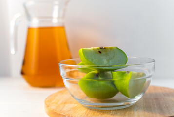 Sliced apple in jar and decanter of juice on white table . Copy space.
