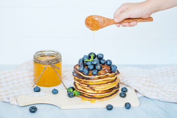 hand pour honey on pancakes with blueberries