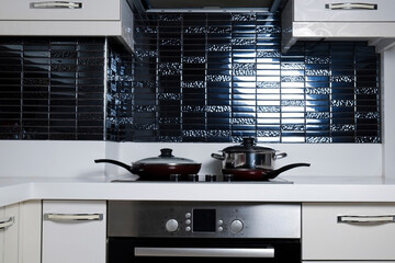 Frying pan on modern black induction stove. Energy efficient electric hob with built-in oven at...