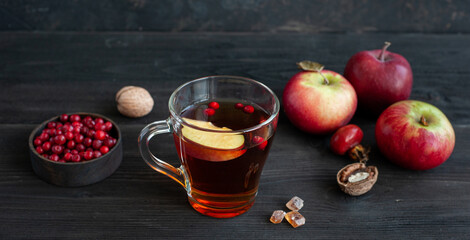 A cup of hot tea on a dark wooden background. Warming drink with berries, cinnamon and apple. Autumn snack with nuts.