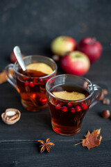 Two cups of autumn warming tea with berries and pieces of apples on a black wooden background. Hot berry tea.