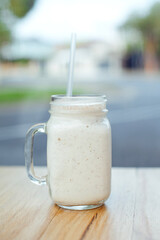 Milk shake cocktail in a glass bottle staying on the table in a cafe. Outside. 