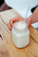 Detail of the handsome man holding milk shake cocktail in a glass bottle with a straw in a cafe. Outside. 