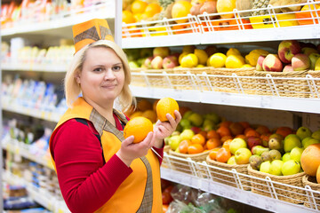 The saleswoman in the supermarket near the shelf with fruit.The seller in a supermarket with three hands