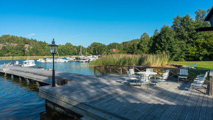 Lounge area for rest and relaxation on a wooden pier near a private residence. White outdoor furniture: table and chairs for meditation watching the sea and sunset. Yachting people luxury lifestyle. 
