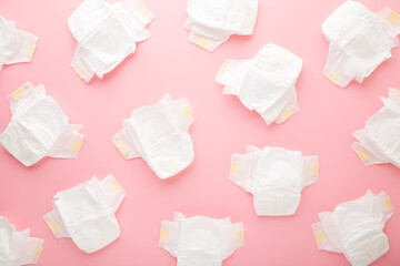 Many white baby diapers on light pink table background. Pastel color. Top down view.