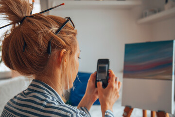 Beautiful artist woman painting in her room while talking on a cellphone.