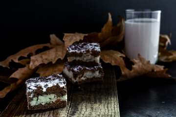 Autumn decor with milk chocolate cookies, a glass of milk and autumn leaves on a black background.