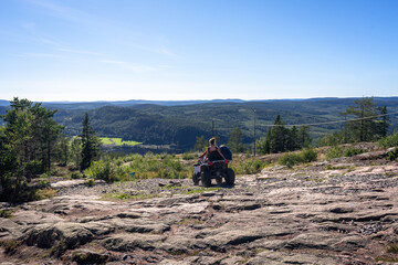 A couple of tourists on a Quad bike ride on Skuleberget mountain in Sweden. Panorama of the Coast of "Hoga Kusten" and the Gulf of Bothnia on a sunny summer day. Travel within the country.