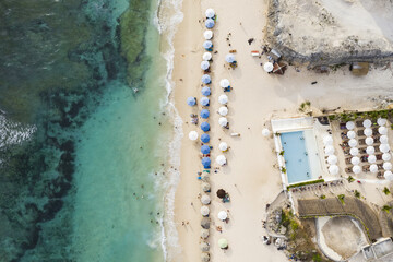 View from above, stunning aerial view of some tourists sunbathing on a beautiful beach bathed by a turquoise sea during sunset, Melasti Beach, South Bali, Indonesia.