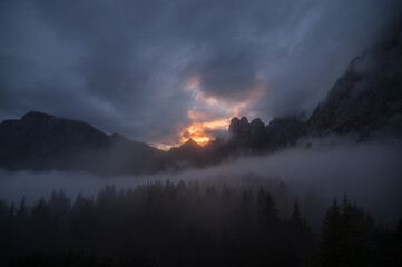 Fototapeta premium Dramatic sunset over Civetta and Moiazza mountain groups on a foggy and cloudy evening as seen from Rifugio Bruto Carestiato, stage 10 of Alta Via 1 trek, Zoldo Dolomites, South Tirol, Italy.