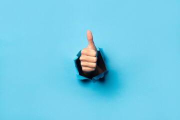 Hand makes thumbs up gesture on blue background. The gesture is all good, like