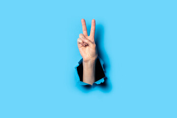 Hand makes a two fingers up gesture on a blue background. Welcome gesture