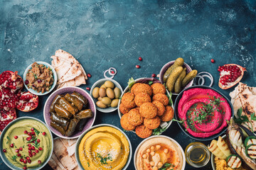 Traditional Middle Eastern assorted meze: hummus, pita, olives, pistachios, dolma, falafel balls, pickles, babaganush, vegetables, pomegranate, eggplants. Top view. Banner. Copy space. Arab meal