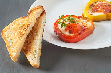 Served dish of bell pepper rings stuffed of fried eggs near toasts in restaurant on concrete table....