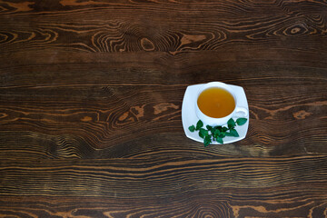 White tea pair with herbal tea stands on a wooden table. View from above. Fresh green leaves and sprigs of mint lie on a saucer. Wood texture. Place for your text.