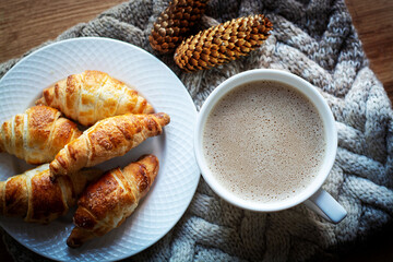 Black coffee with milk and croissants. Coffee beans on a wooden table. Knitted wool scarf in the background.
