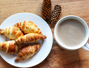 Black coffee with milk and croissants. Coffee beans on a wooden table. Knitted wool scarf in the background.