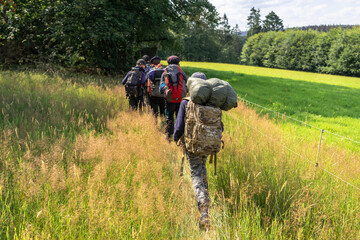 Scouts or tourists go with big backpacks on the green forest trail on sunny summer day. Active...