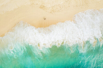View from above, stunning aerial view of a couple relaxing on a beautiful beach bathed by a turquoise sea during sunset. Kelingking beach, Nusa Penida, Indonesia.
