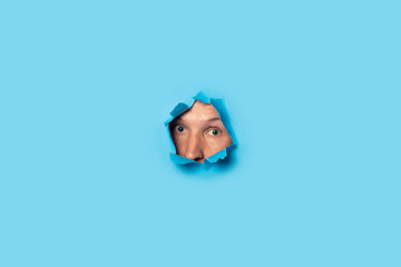 Man looks out and looks out of the hole on a blue background. Listen, spy, wiretapping
