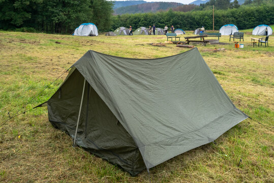 Scout camping. Army military tent close up in the base camp. Lots of  tents stand on a field against a green forest. 