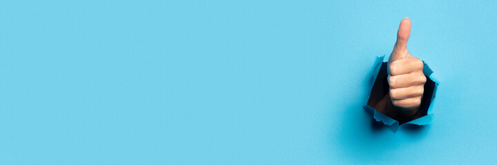 Hand makes thumbs up gesture on blue background. The gesture is all good, like