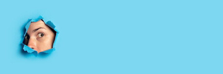 Woman peeps and looks out of the hole on a blue background. Listen, spy, wiretapping